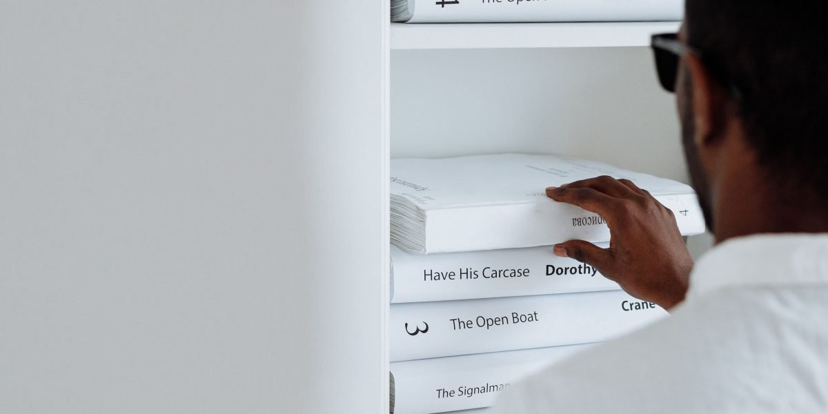 A person's hand reaching for a book on a crowded shelf, symbolizing the active choice in seeking self-help resources.